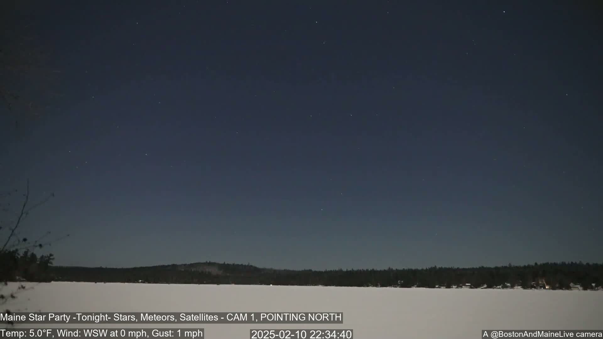 A mostly clear night sky with a few stars visible over a snow-covered landscape and dark trees under a 5°F temperature with a light west-southwest wind.