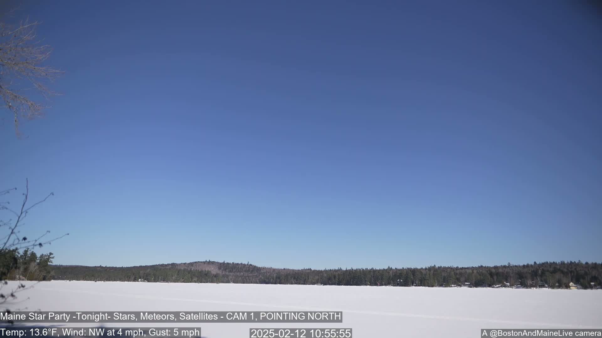 A snow-covered lake stretches to a treeline under a clear blue sky, with a light northwest wind.