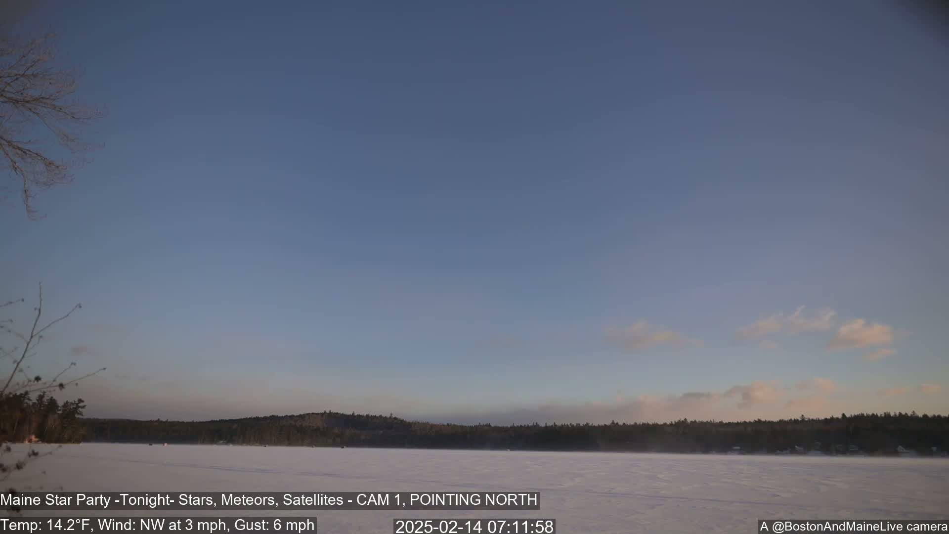 A frozen lake, under a mostly clear, twilight sky with a light northwest wind, is surrounded by a snow-covered landscape and dark, distant trees.