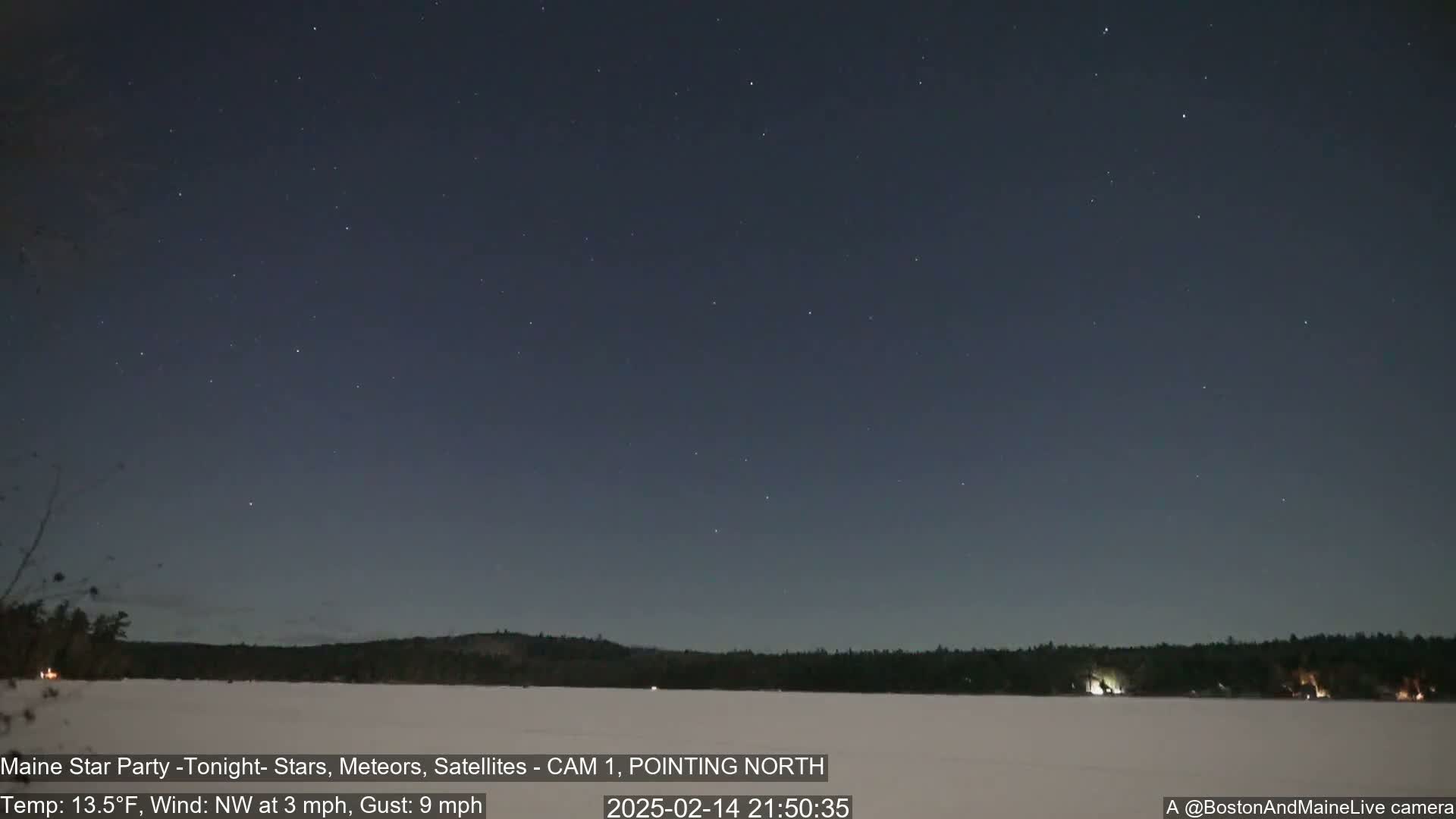 A night sky with numerous stars over a snow-covered lake and a dark treeline, under a northwest wind of 3 mph with gusts up to 9 mph and a temperature of 13.5°F.