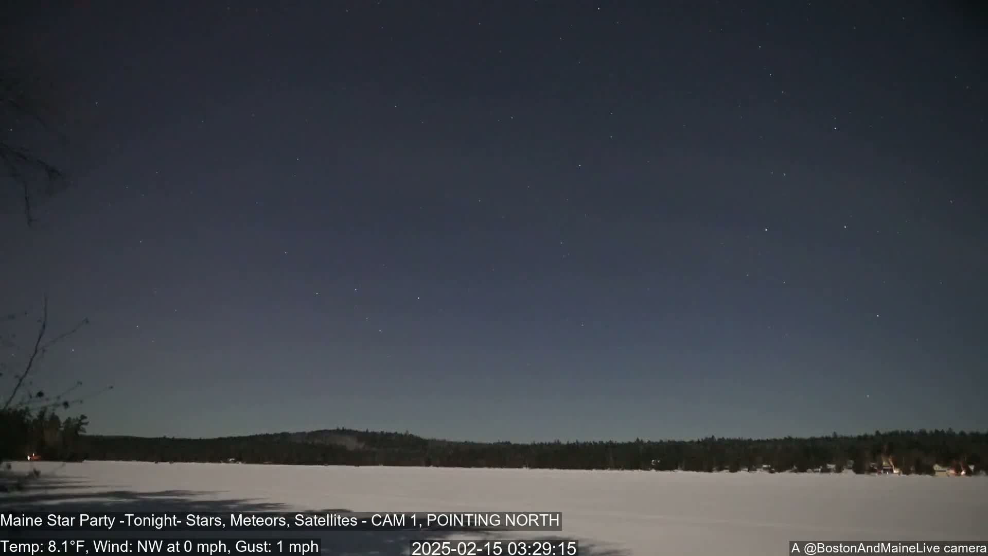 A clear night sky with numerous stars is visible over a frozen lake and a snow-covered treeline.
