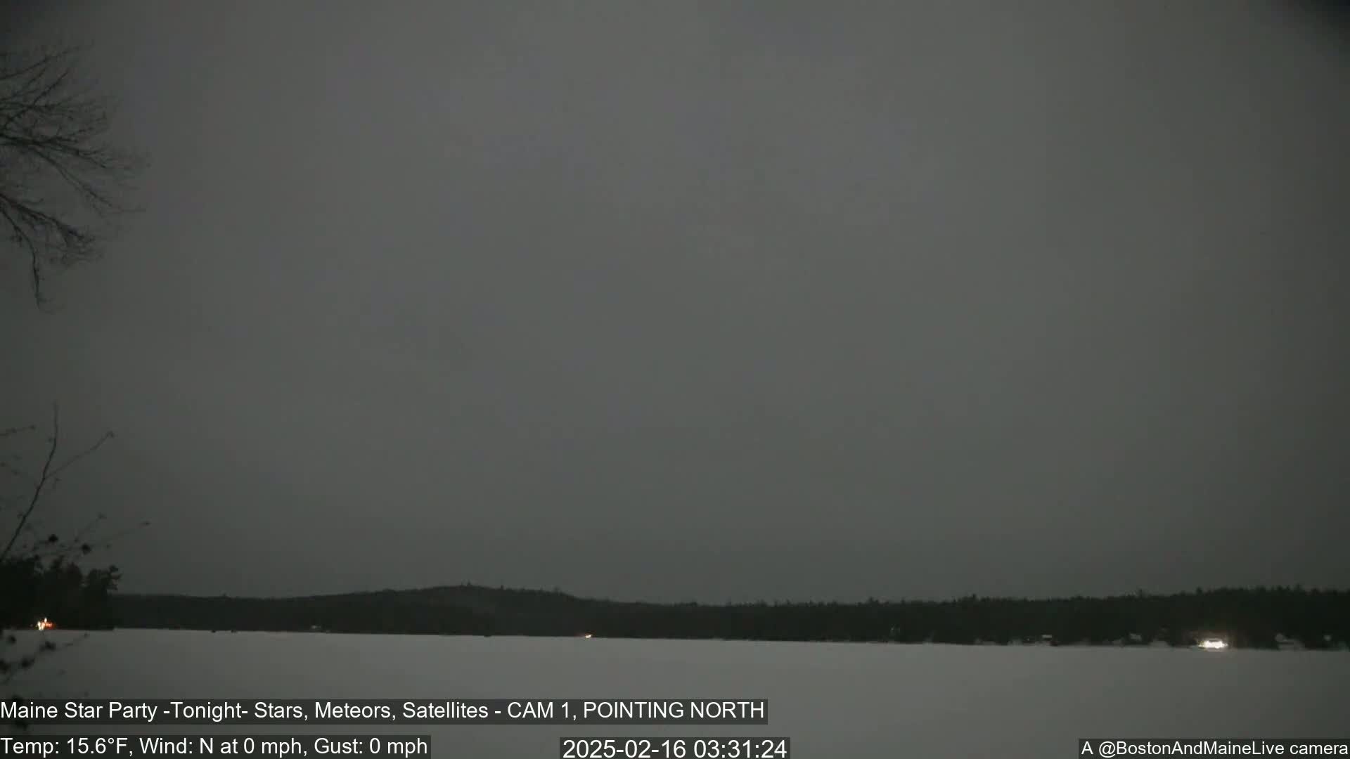 A dark, overcast night scene shows a frozen lake with a treeline in the distance, under a calm, gray sky.