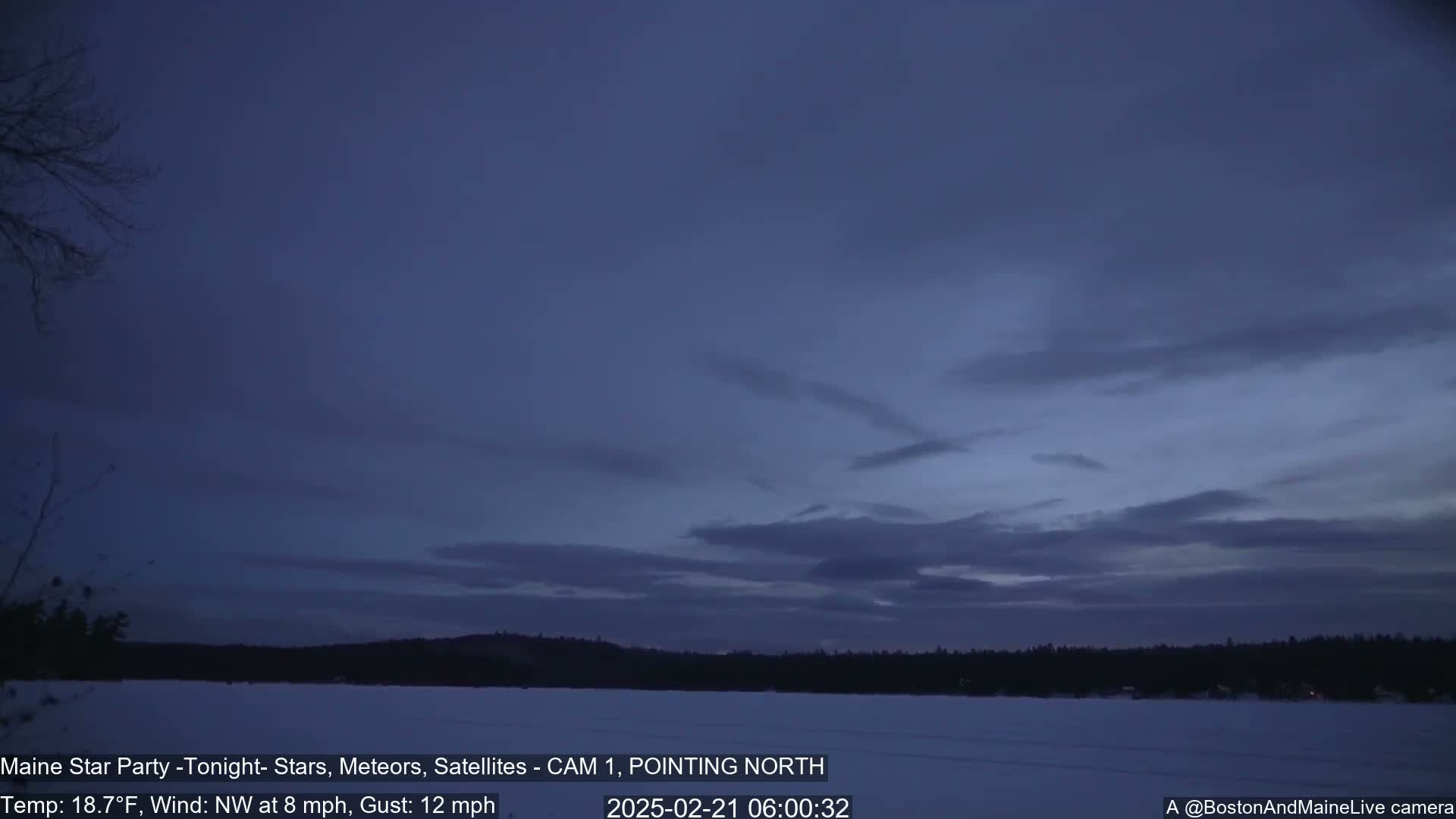 A snow-covered lake is visible under a twilight sky with thin clouds and a northwest wind.
