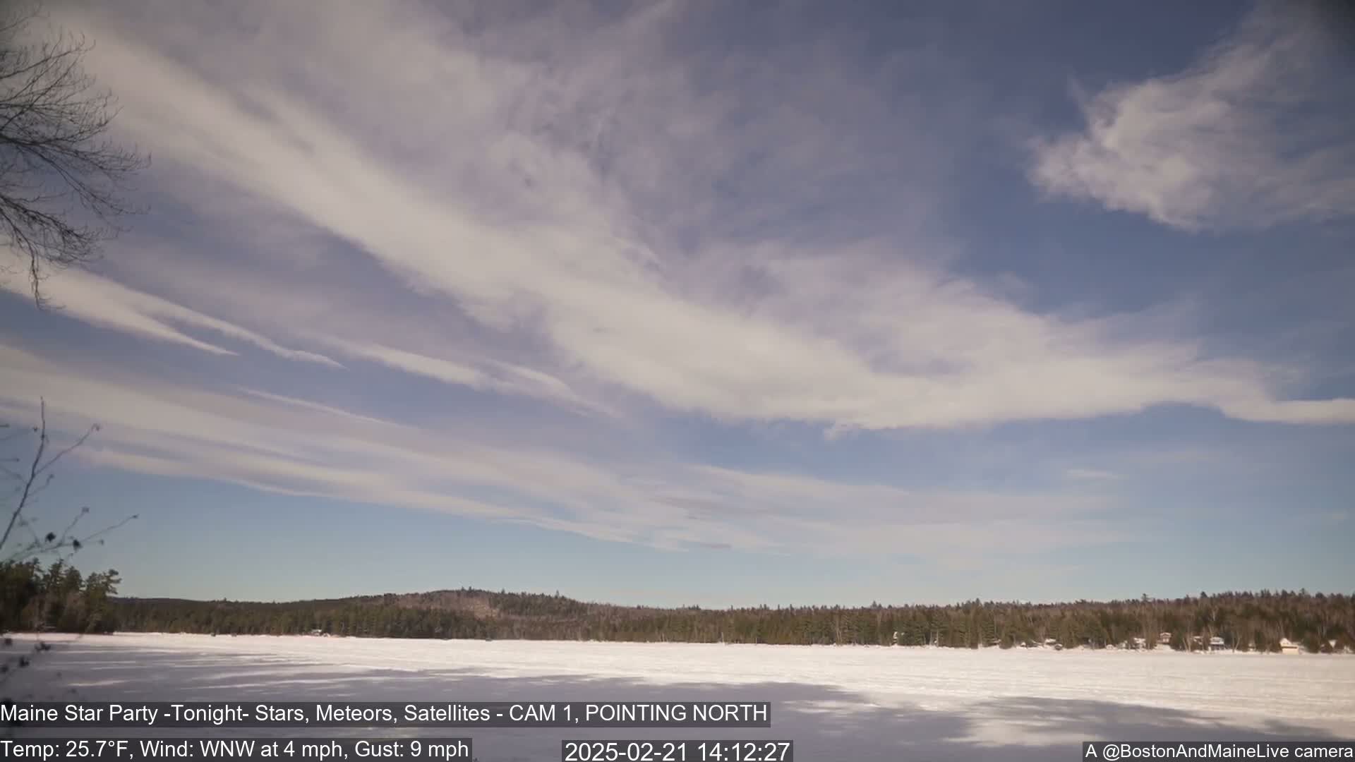 A frozen lake is visible under a mostly clear sky with thin, wispy clouds, and a treeline in the background.