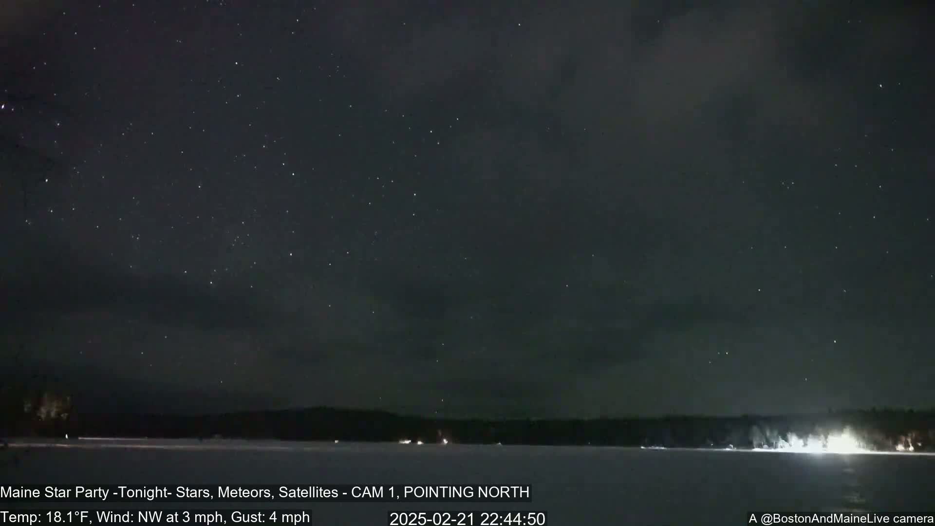 A nighttime view of a starry sky over a snow-covered lake and dark trees, with a calm wind blowing from the northwest at 3 mph, gusting to 4 mph.