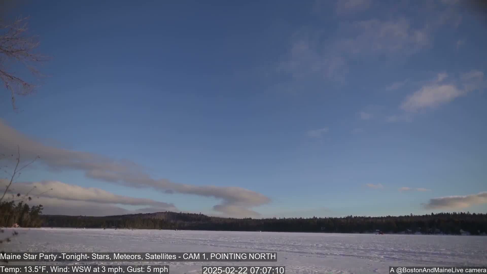 A frozen lake is visible beneath a mostly clear sky with a few wispy clouds, under a calm, cold, and slightly windy weather condition.