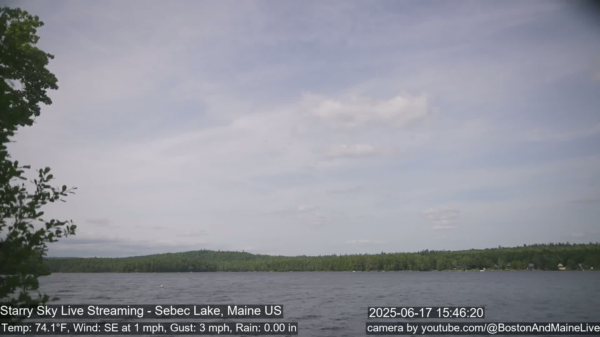 A mostly cloudy sky over a calm lake with a treeline in the background.