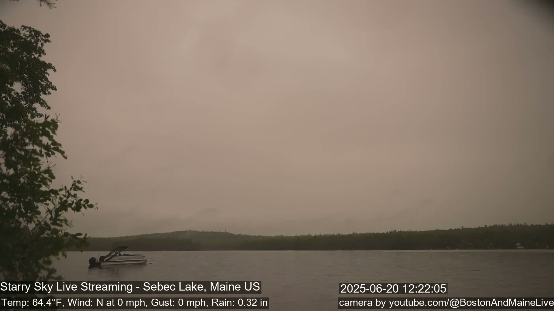 A hazy, light brown sky hangs over a calm lake with a single boat and a treeline in the distance.