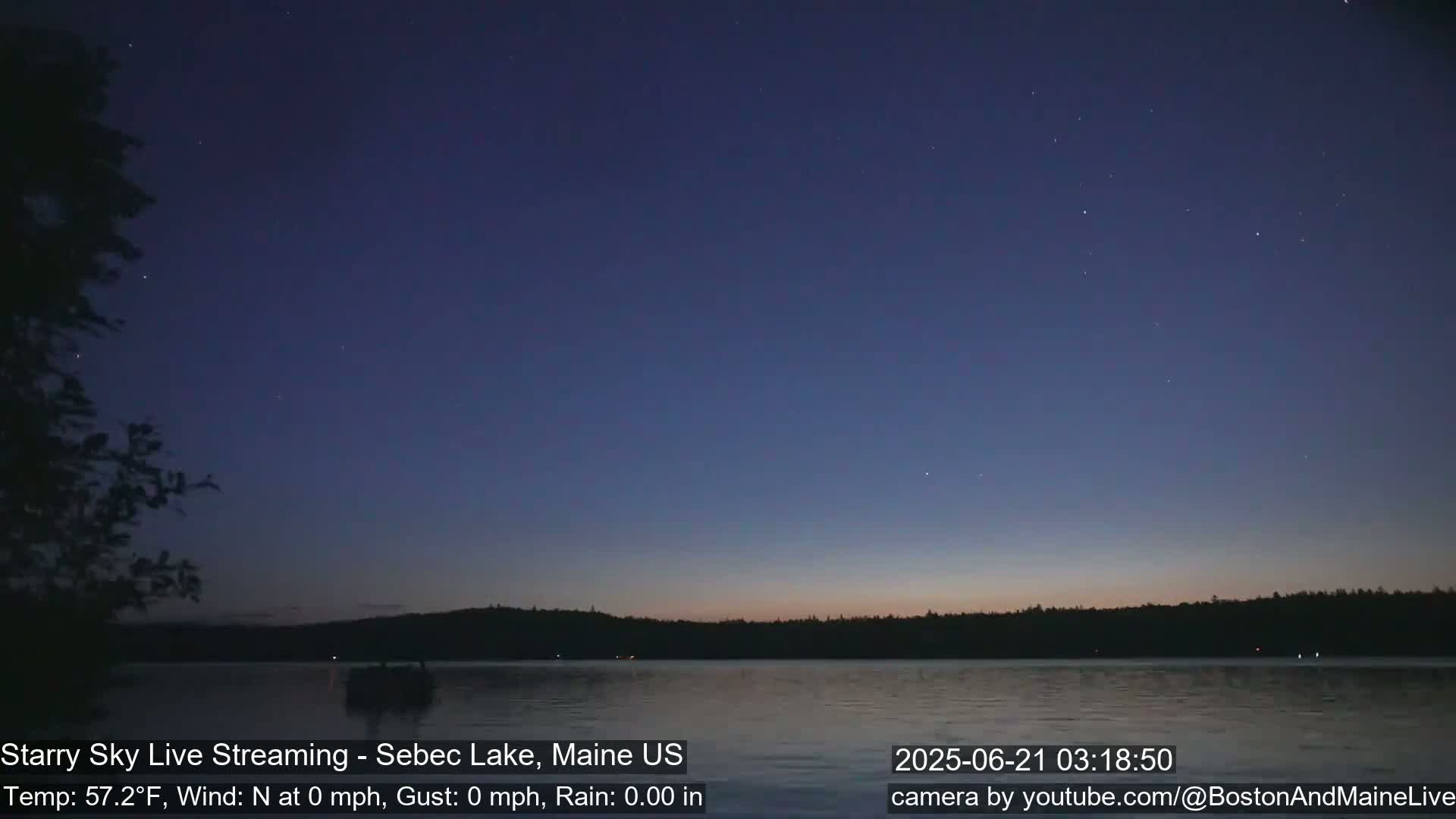 A tranquil lake at twilight is visible under a clear, starry sky.