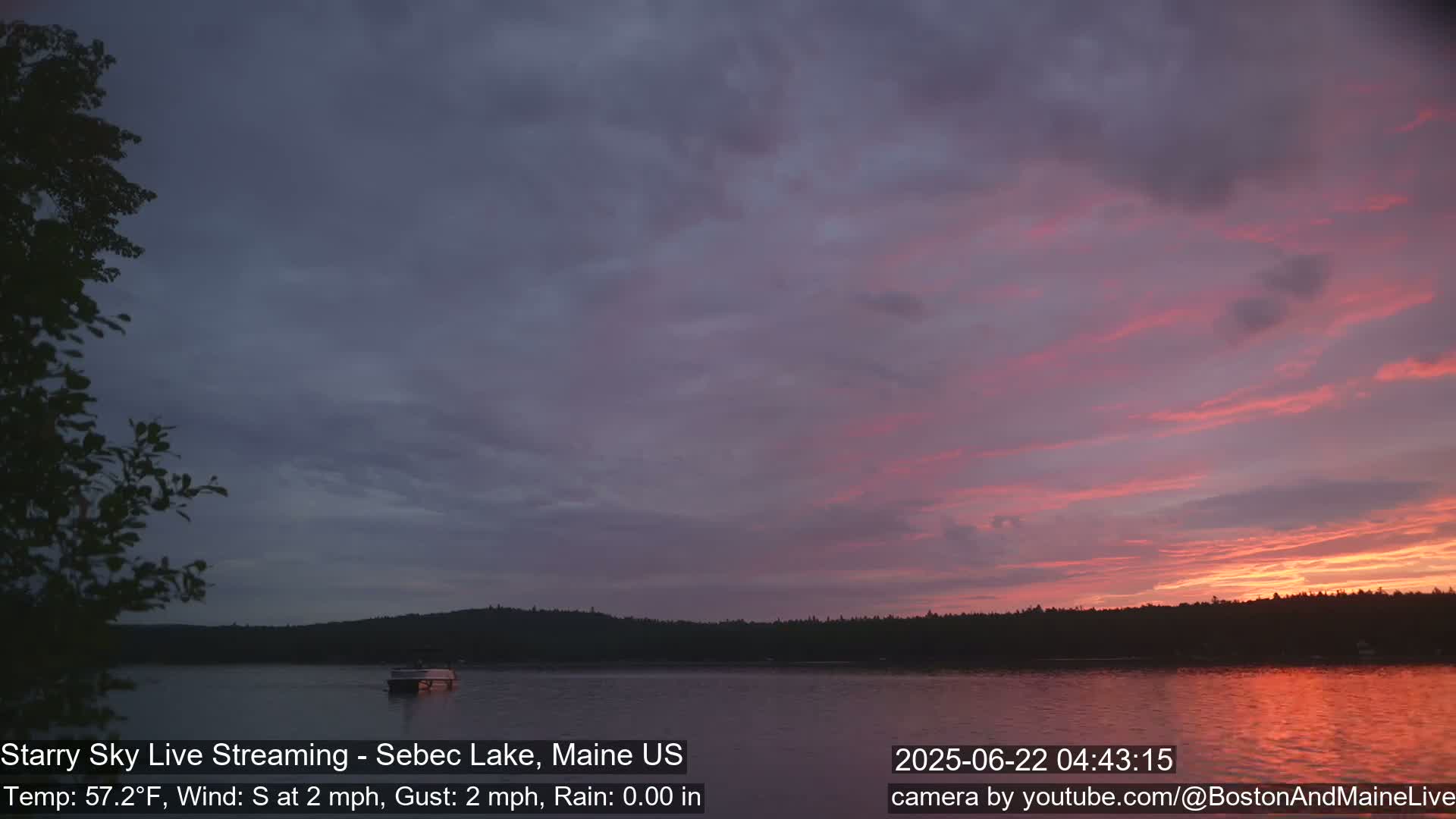 A calm lake at sunset with a boat on the water, under a pink and purple sky with a light southerly wind.