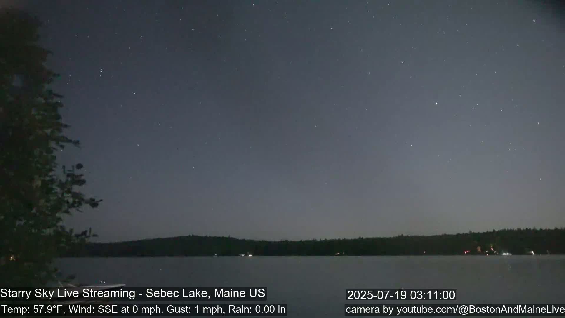 A calm lake is viewed at night under a starry sky with a slight wind.