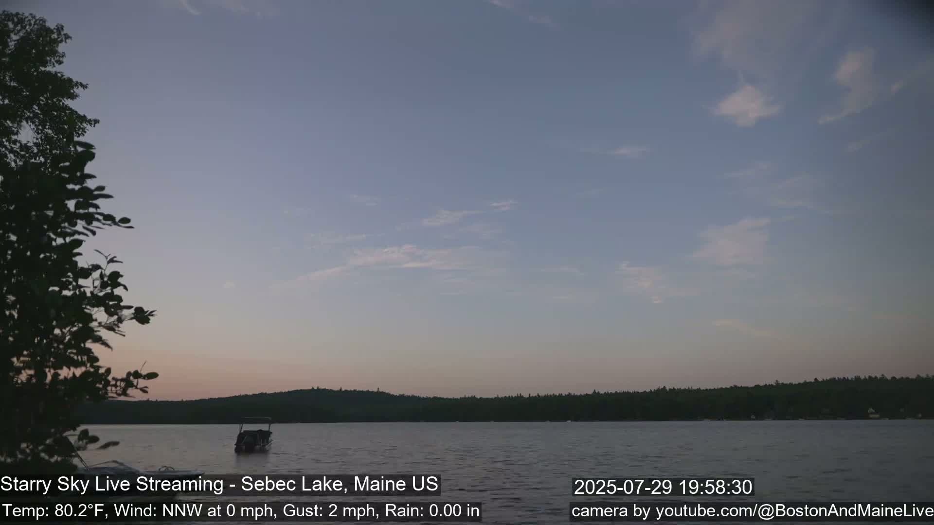 A calm lake is viewed at night under a starry sky with a slight wind.