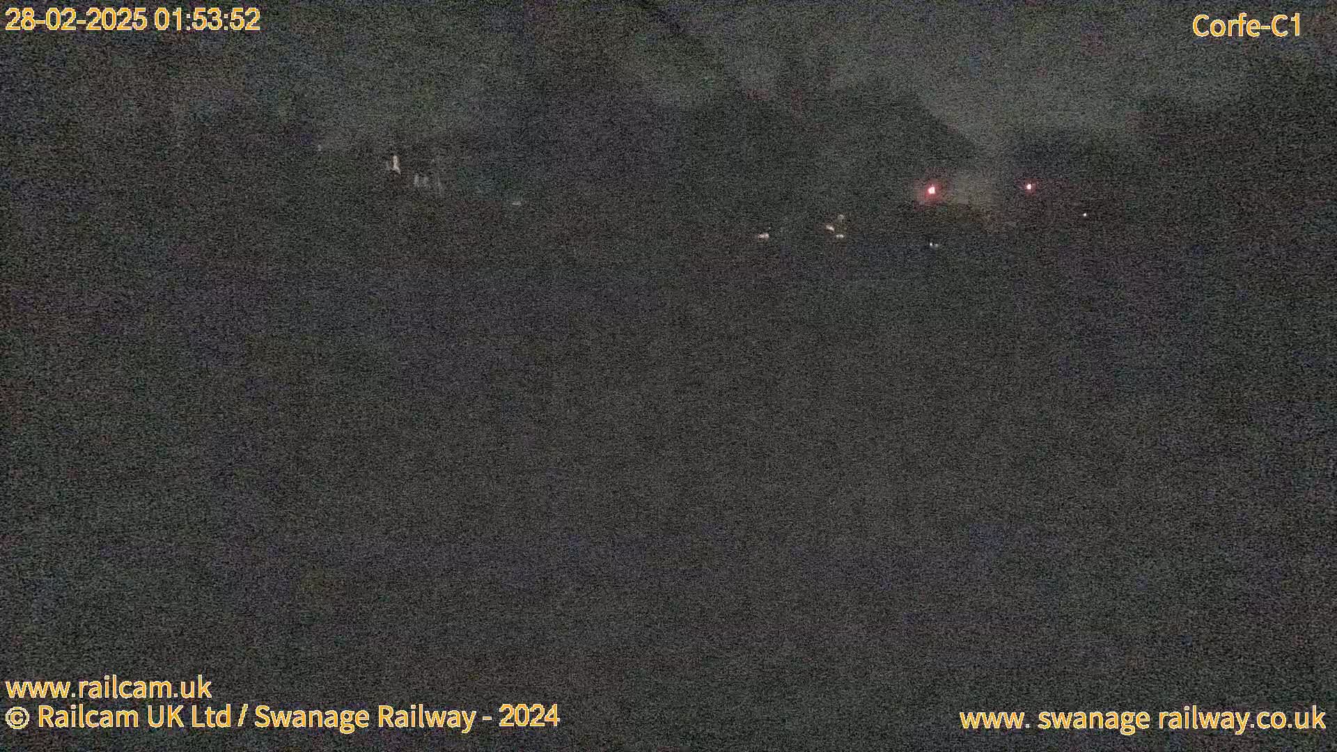 A nighttime, low-light outdoor scene shows a dark landscape with a few faint, distant lights.