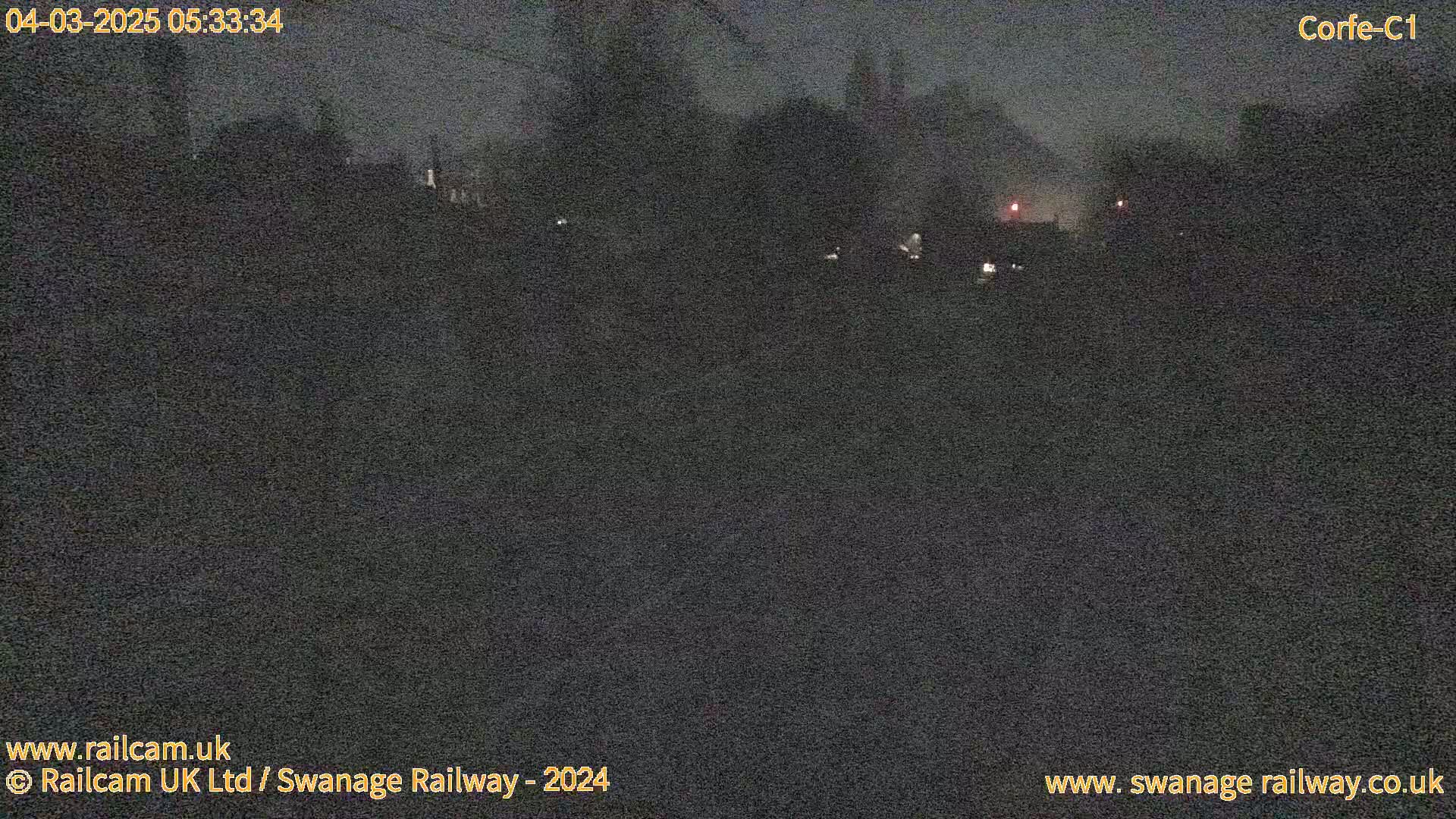 A dark, nighttime view of trees and buildings in the distance, under a mostly cloudy sky.