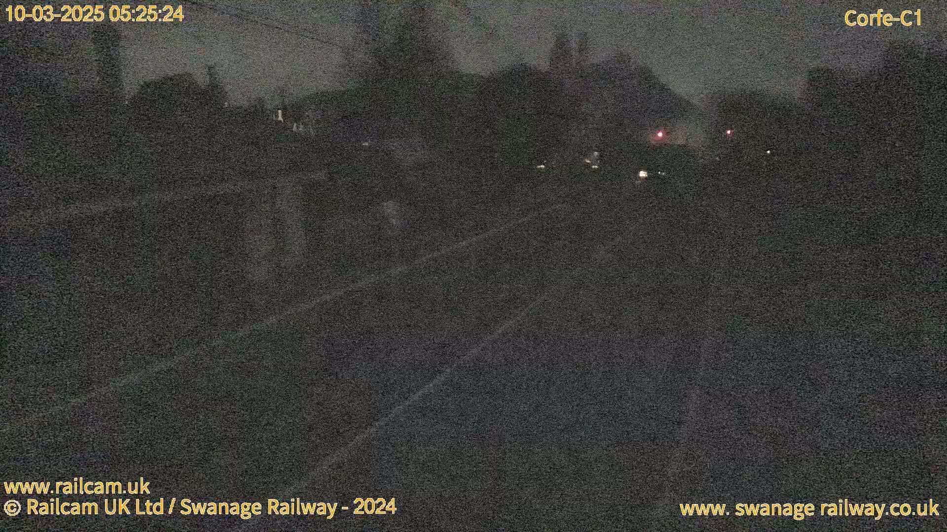 A nighttime, low-light view of a railway track with indistinct shapes of trees and buildings in the background.