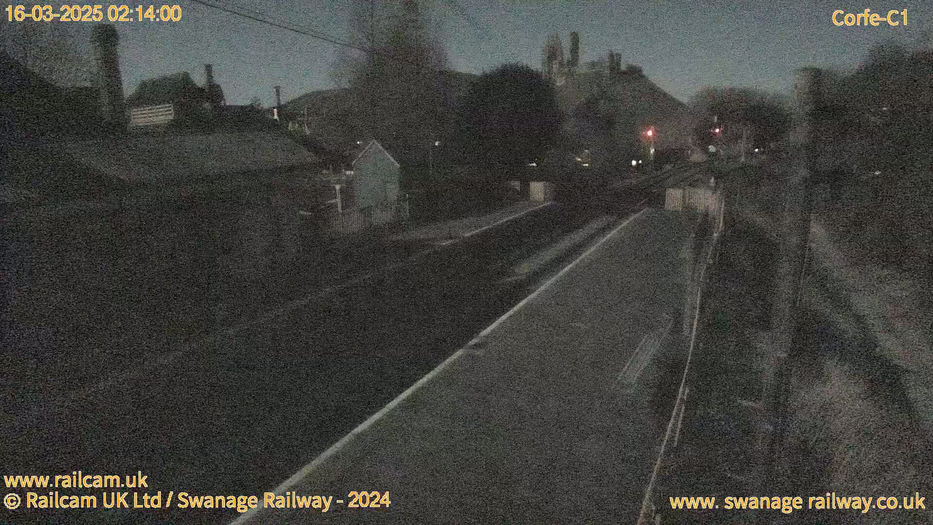 A nighttime view of a train station platform and surrounding buildings under a dark sky.