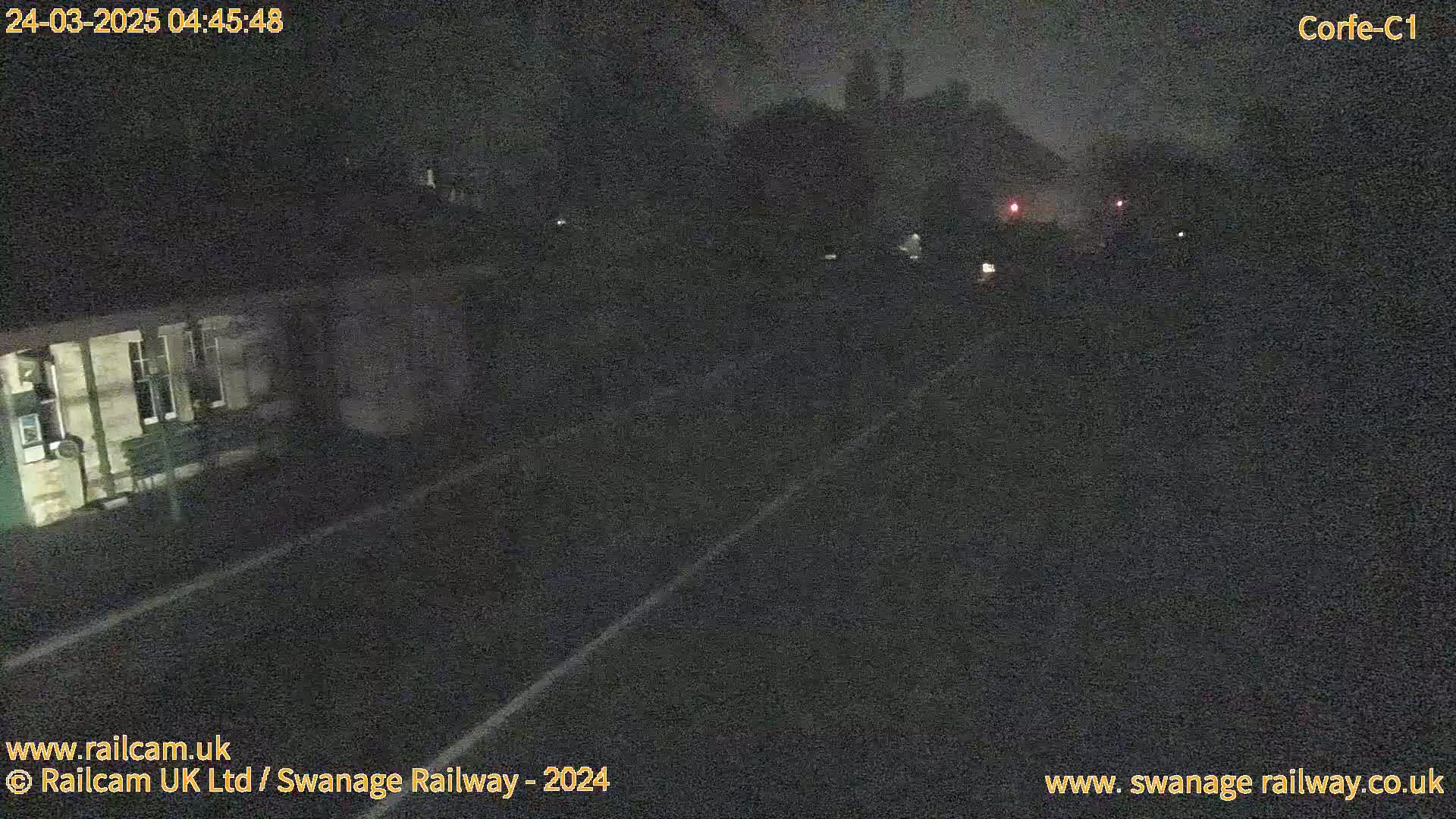 A nighttime view of a railway track and a building, under a dark sky.