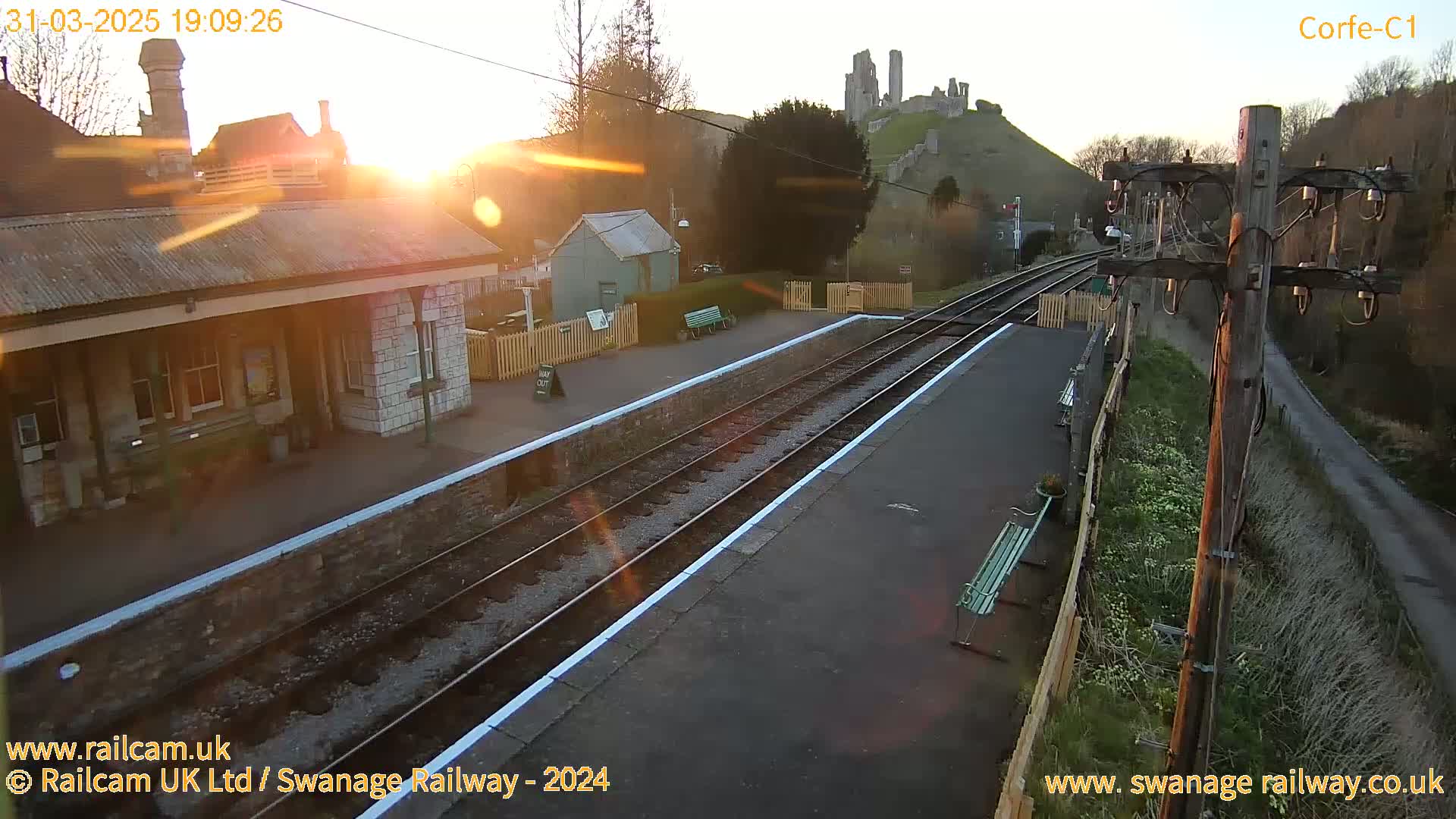 A train station platform at sunrise, with a distant castle visible on a hill.