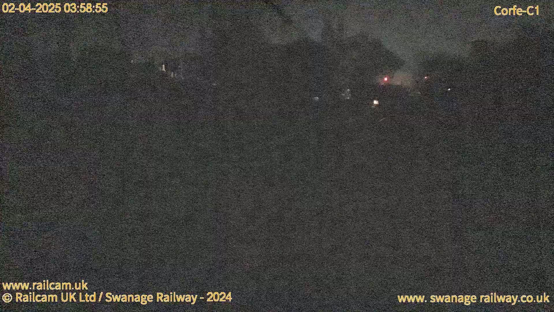 A nighttime, low-light view of a dark, possibly rural landscape with a few faint lights visible in the distance.
