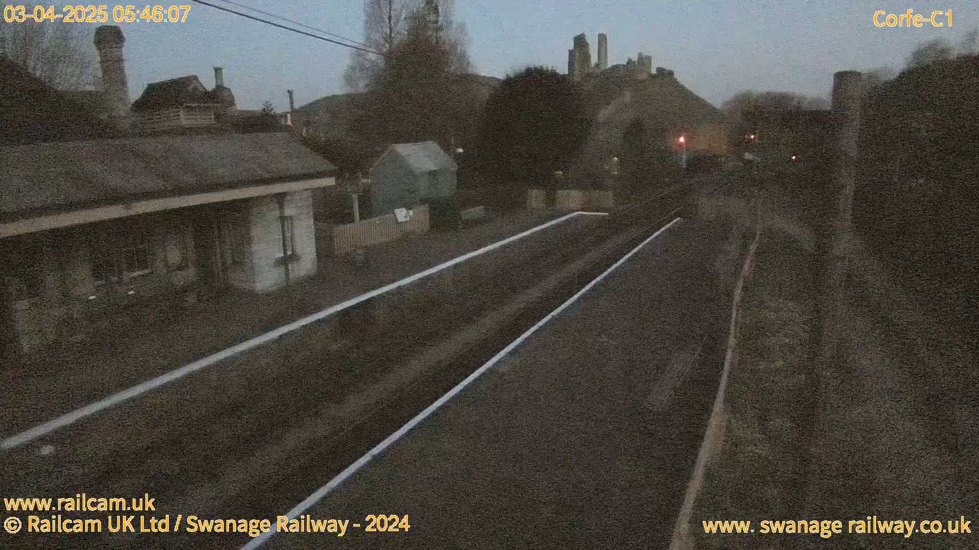 A dimly lit train station platform at dawn, with a castle visible in the distance.