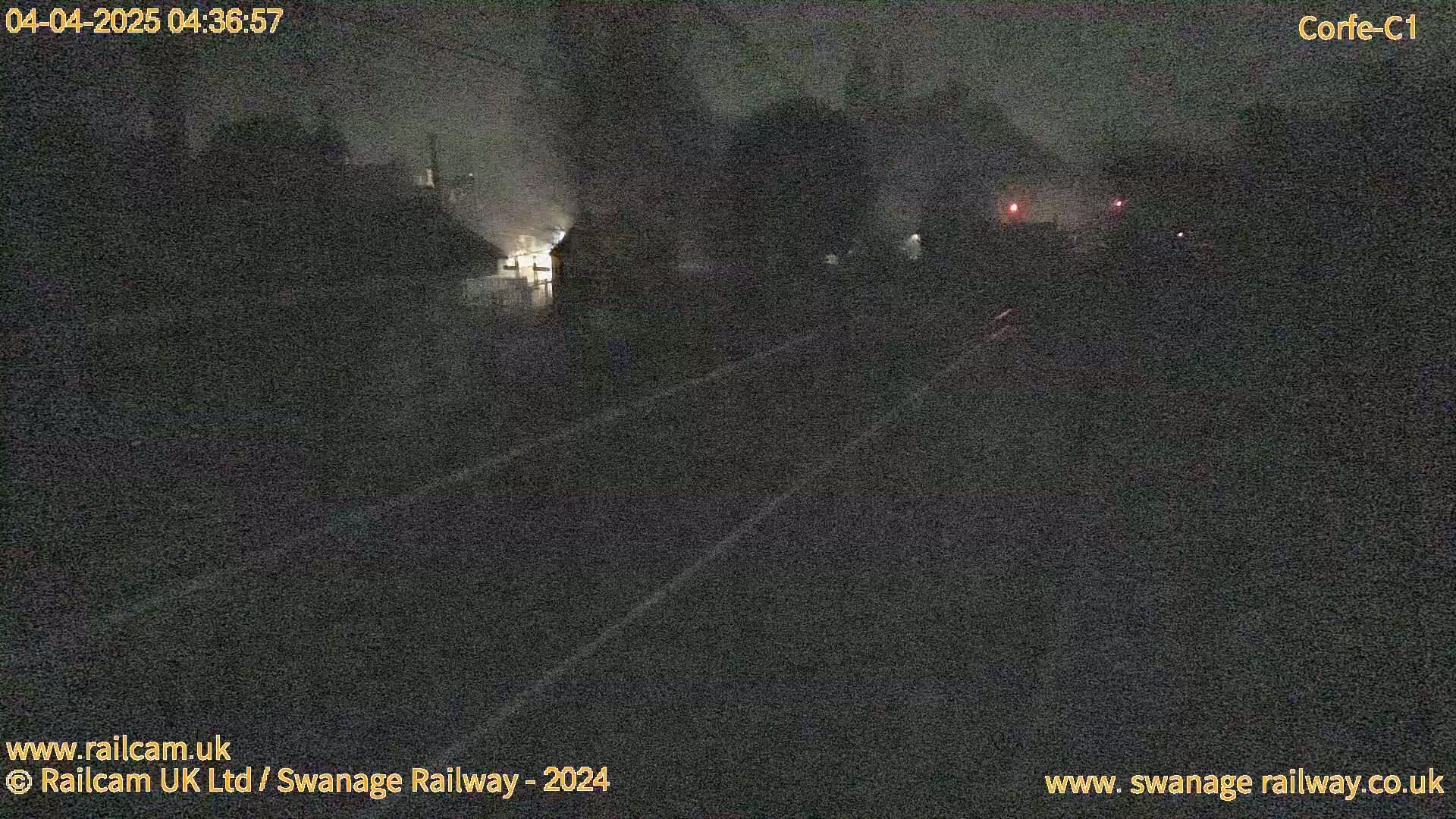 A nighttime, dimly lit view of a railway track and surrounding structures under overcast skies.