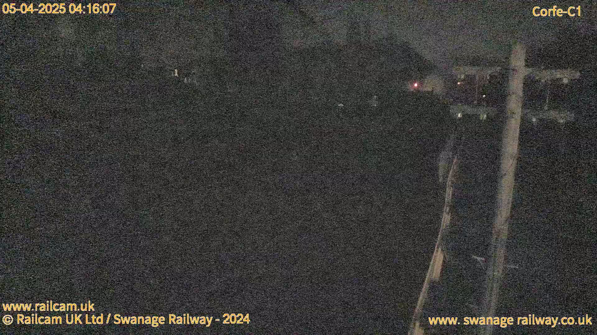 A nighttime, dark outdoor scene shows a utility pole and indistinct shapes in the distance under a dark sky.