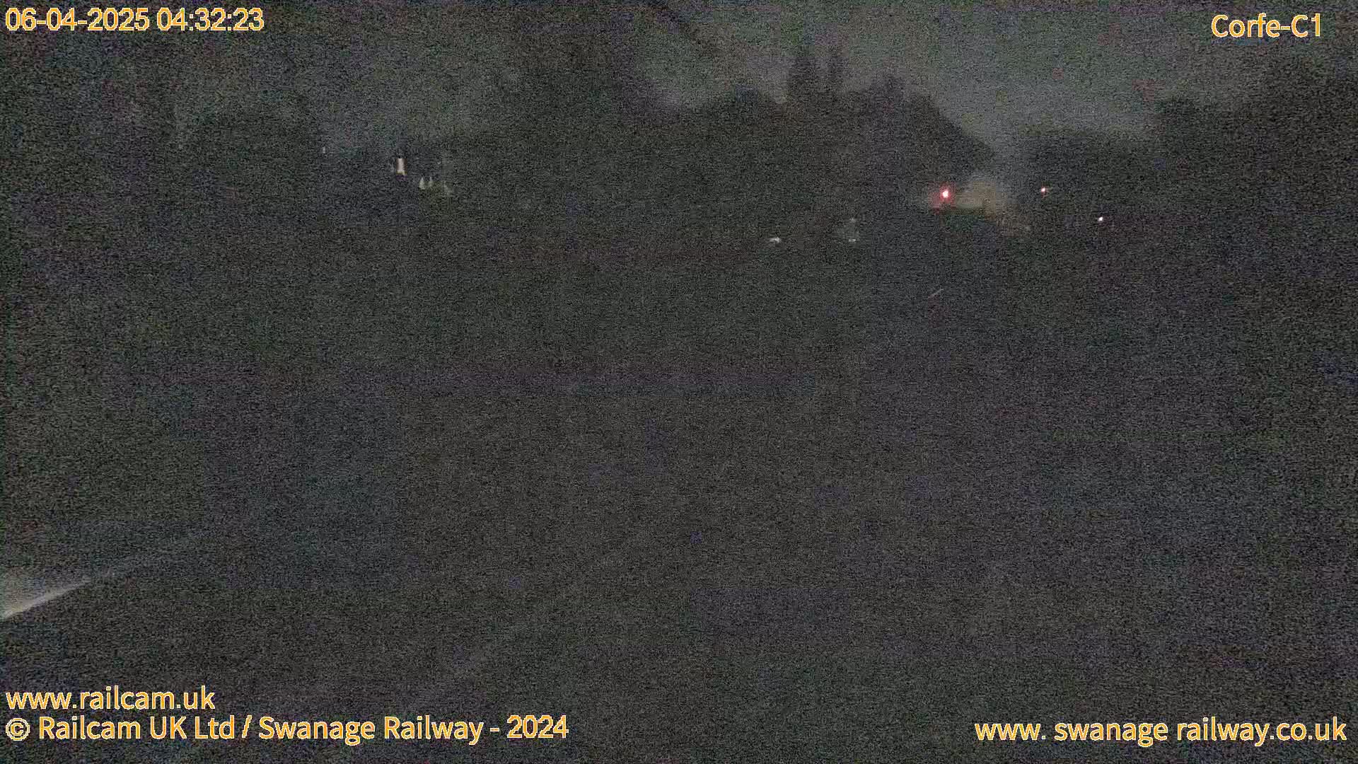 A dark, nighttime scene shows a dimly lit landscape with a few faint lights in the distance.