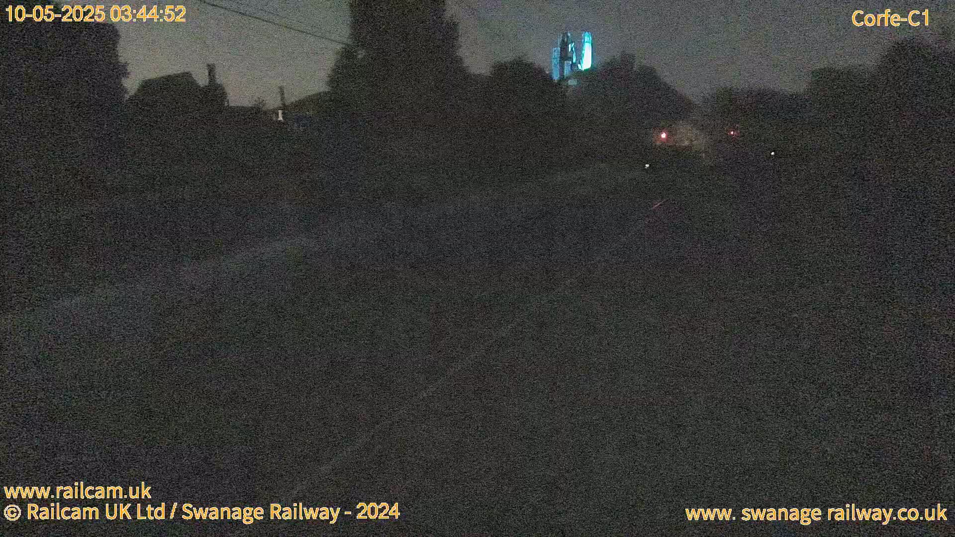 A dark, nighttime view of a road, with indistinct buildings and some faint lights in the distance.