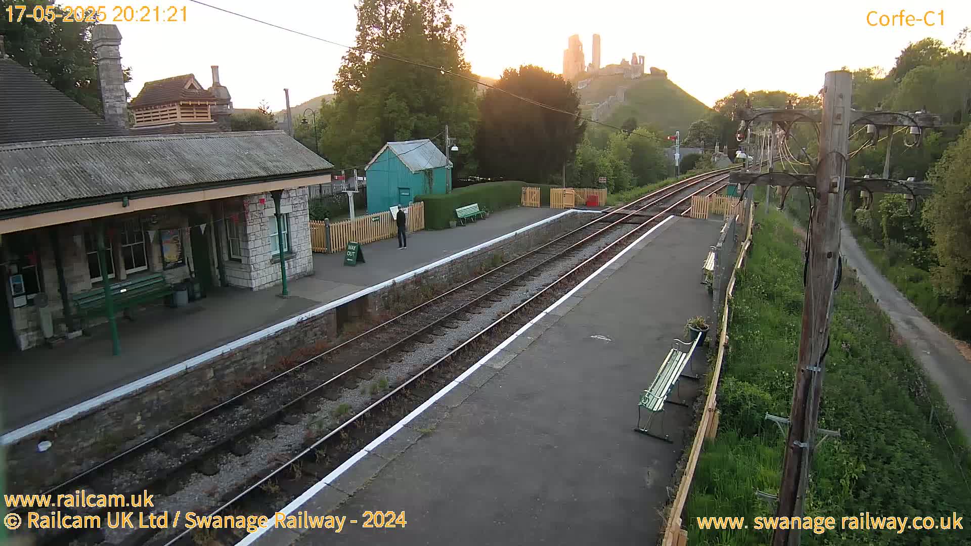 A train station platform with a stone building and a castle in the background at sunrise.