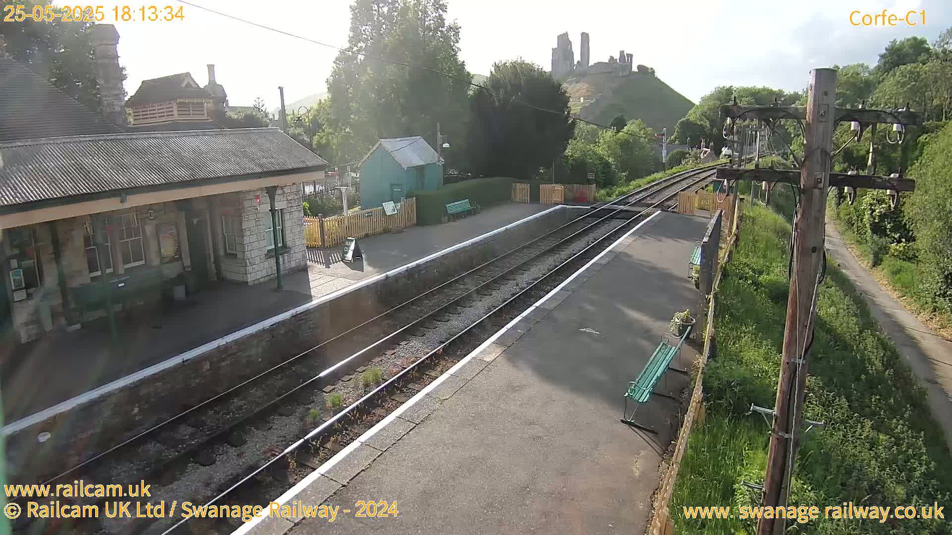 A train station platform with a stone building and a view of a castle ruin on a sunny day.