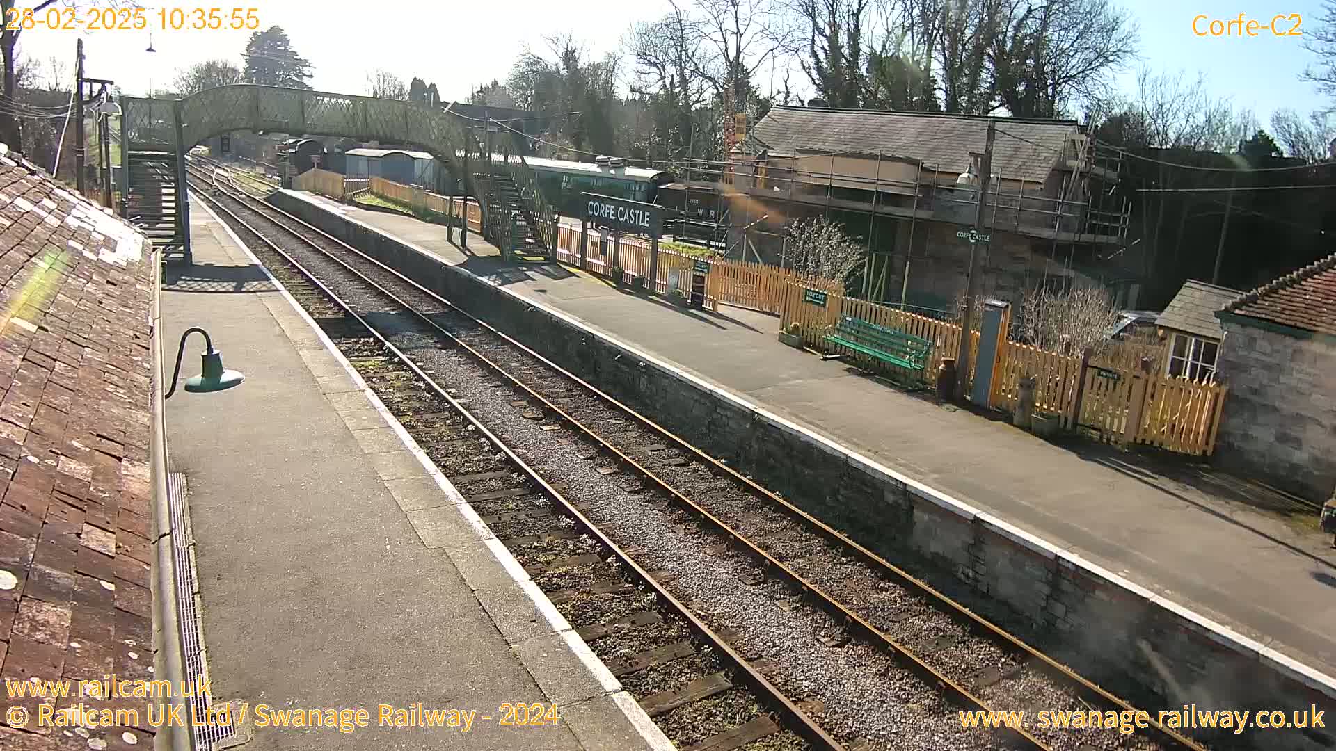 A sunny day at a train station with a railway track, platform, and station buildings, one of which is under construction.