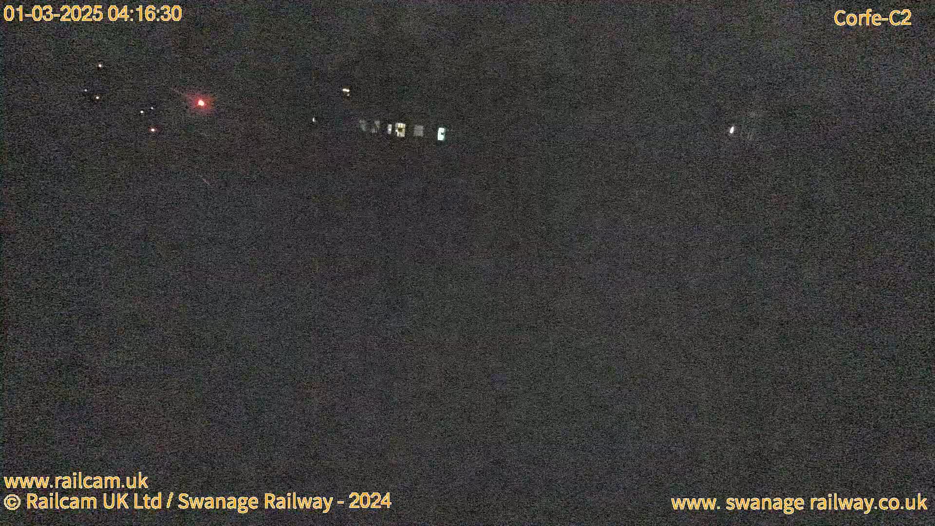 A nighttime, dark view of a sparsely lit area with a few distant lights visible.