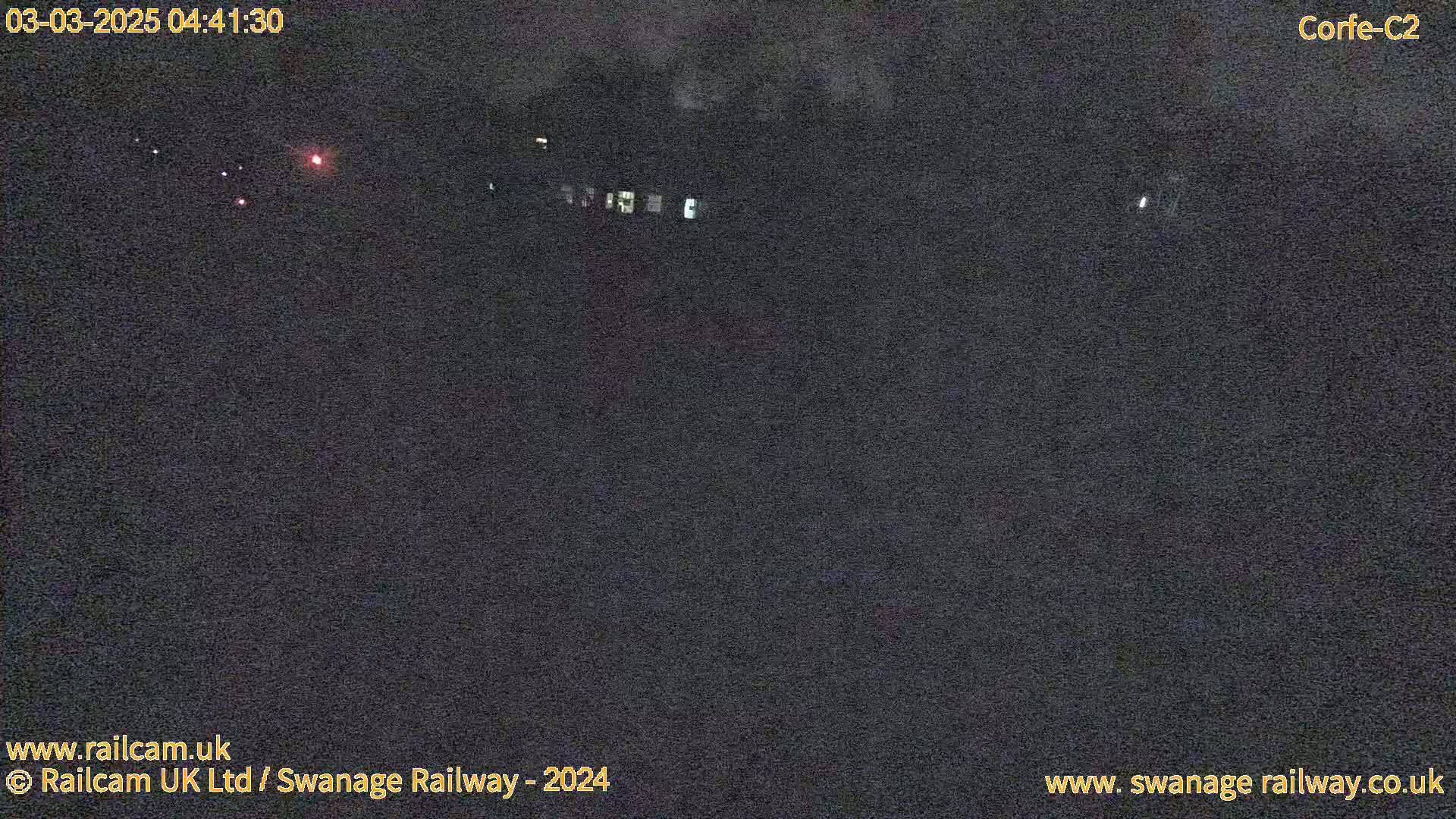 A nighttime, low-light view of a dark landscape with a few distant lights.