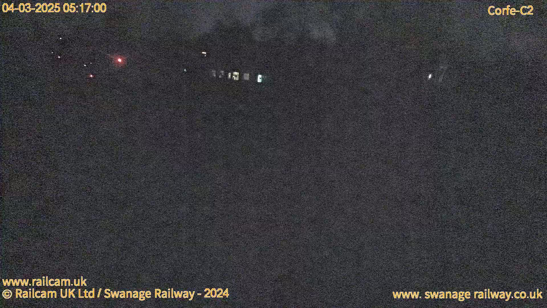 A nighttime, outdoor scene shows a dark, mostly featureless expanse with a few faint lights in the distance.