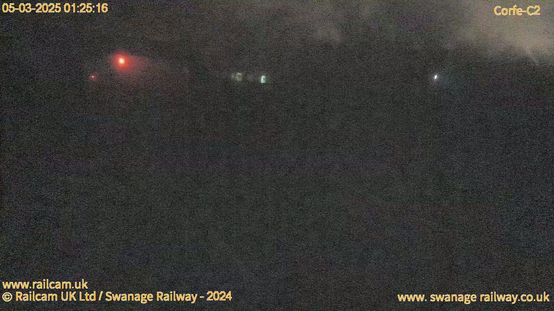 A nighttime, dark outdoor scene shows a few faint lights in the distance under a cloudy sky.