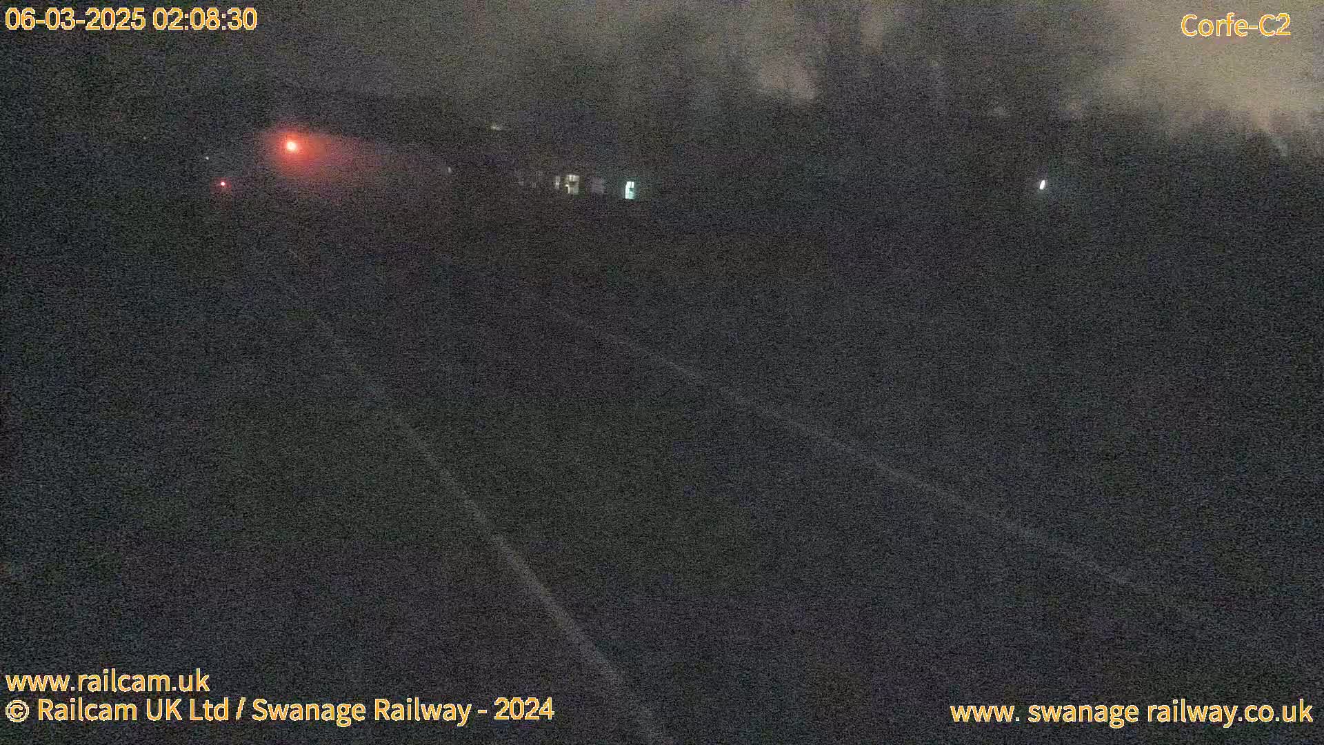 A dark, nighttime scene shows a roadway with a faint, distant light source and what appears to be fog or mist.