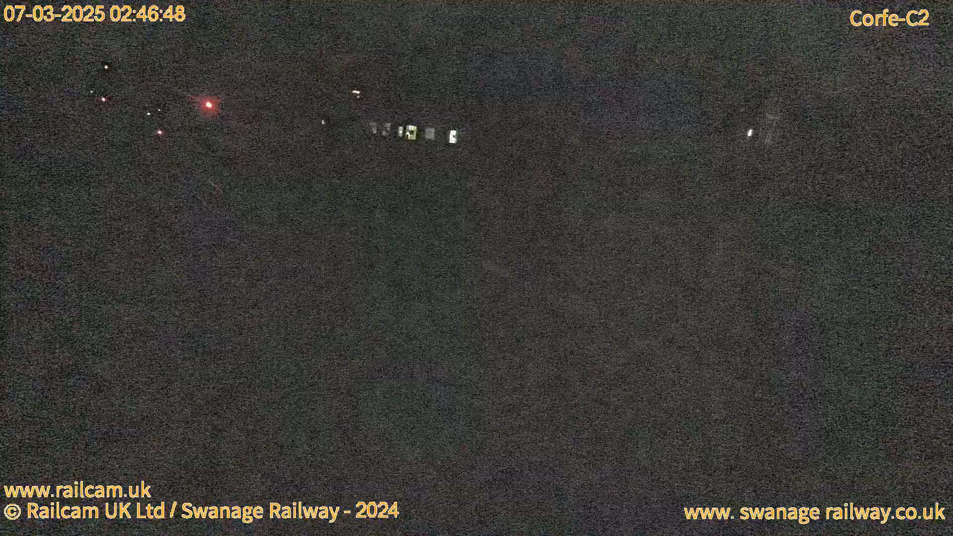 A dark, nighttime scene shows a few distant red and white lights along a dark expanse.