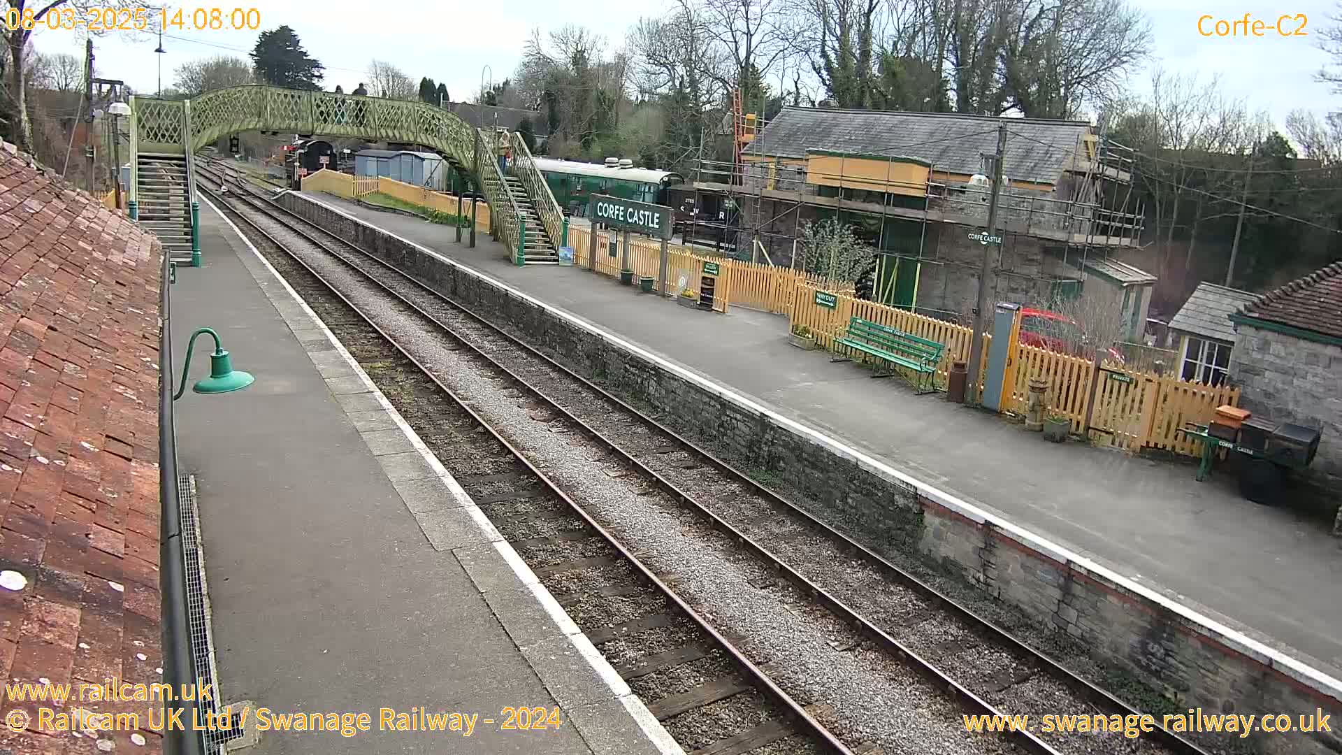 A railway station platform with a train and railway buildings under partly cloudy skies.