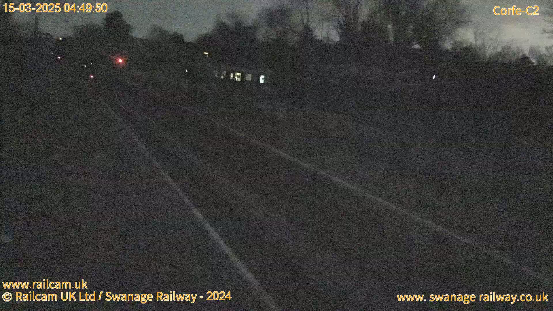 A dark, nighttime view of a railway track extending into the distance, under a cloudy sky.