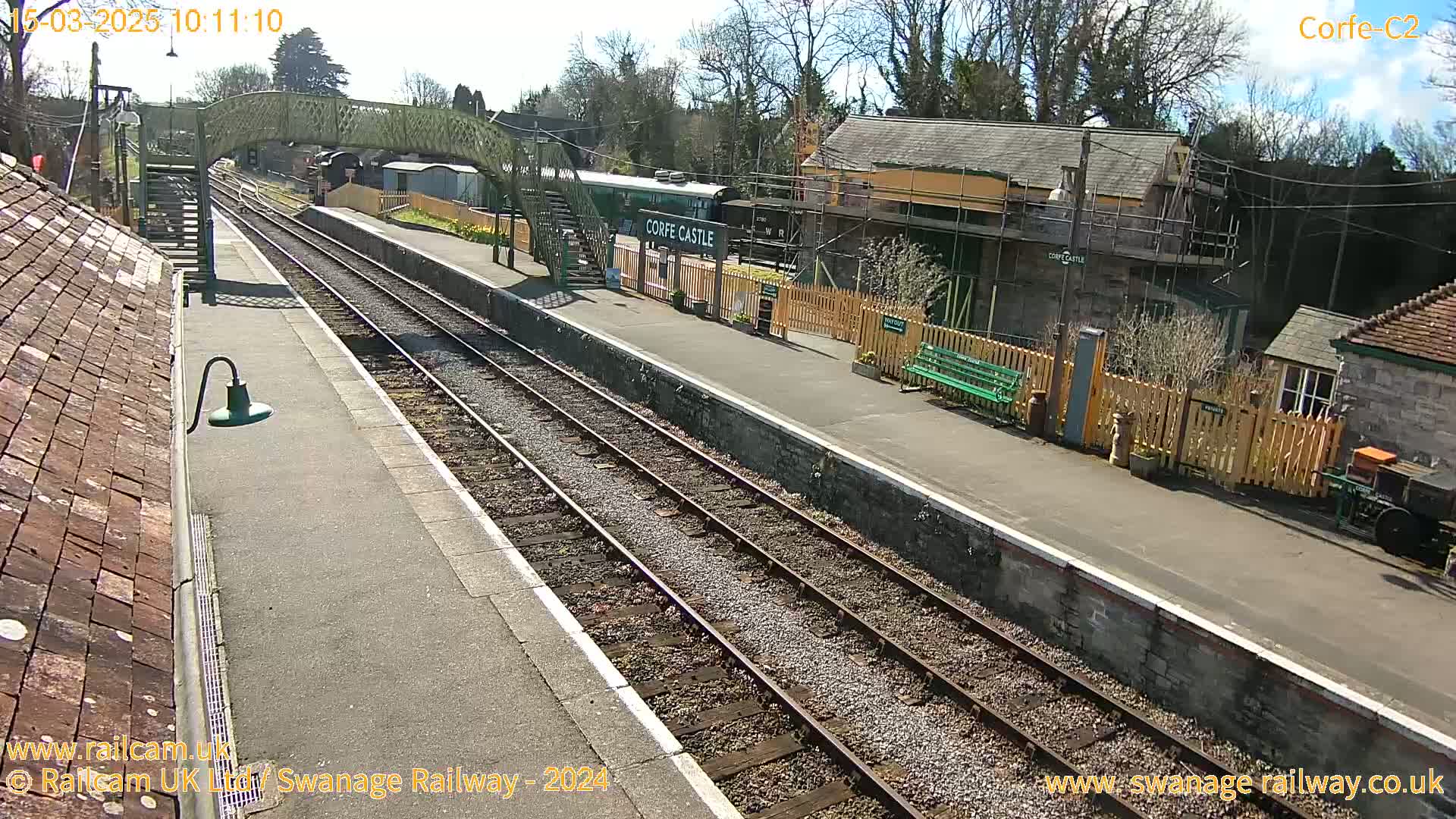 A sunny view of a train station platform with train tracks, a train car, and several buildings.