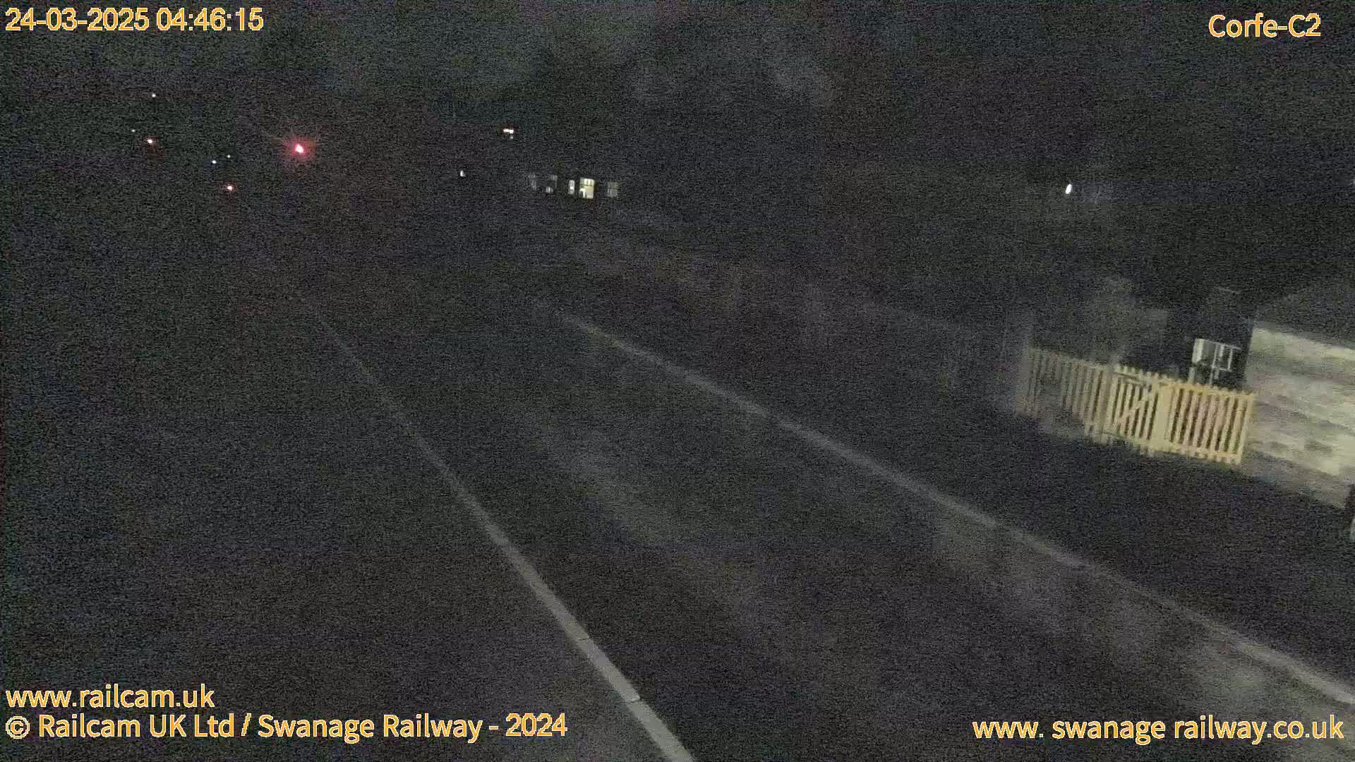 A dark, nighttime road scene shows a paved road with faint white lines and dim lights in the distance.