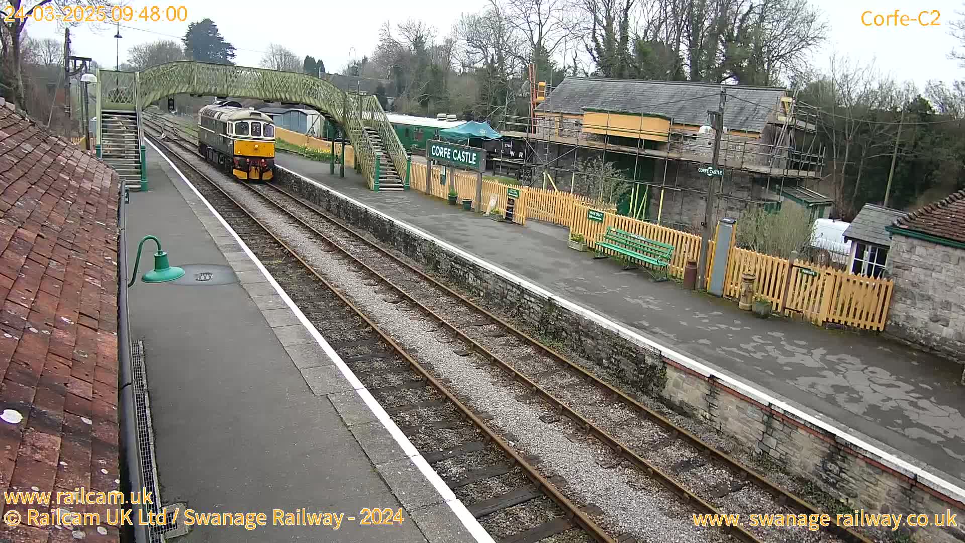 A diesel train departs from a railway station on an overcast day.
