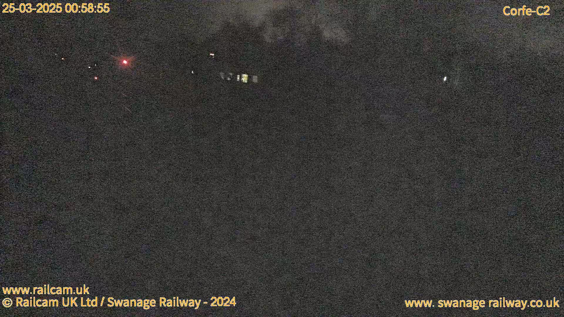 A dark, nighttime scene shows a few faint lights in the distance under a cloudy sky.