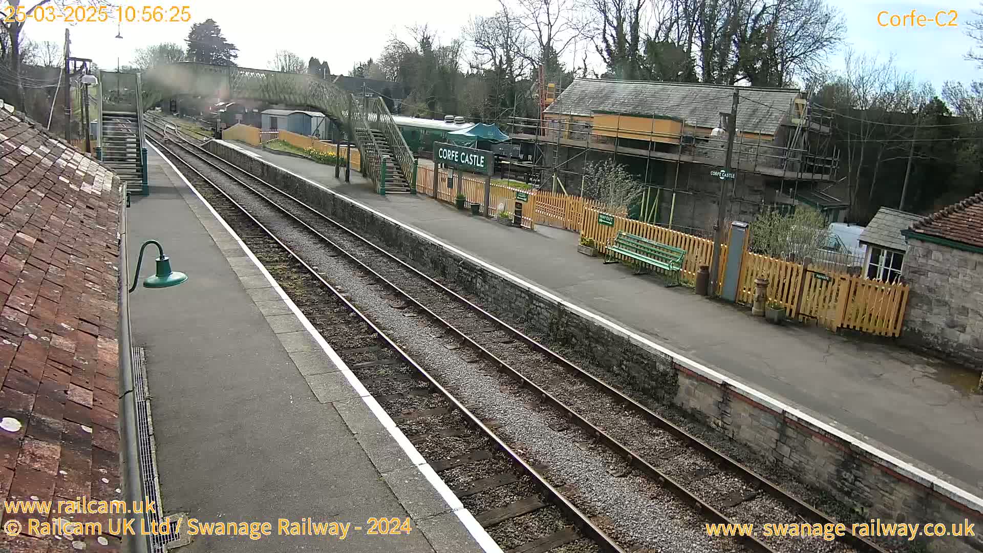 A train station platform with train tracks, a partially-constructed building, and a partially sunny day.