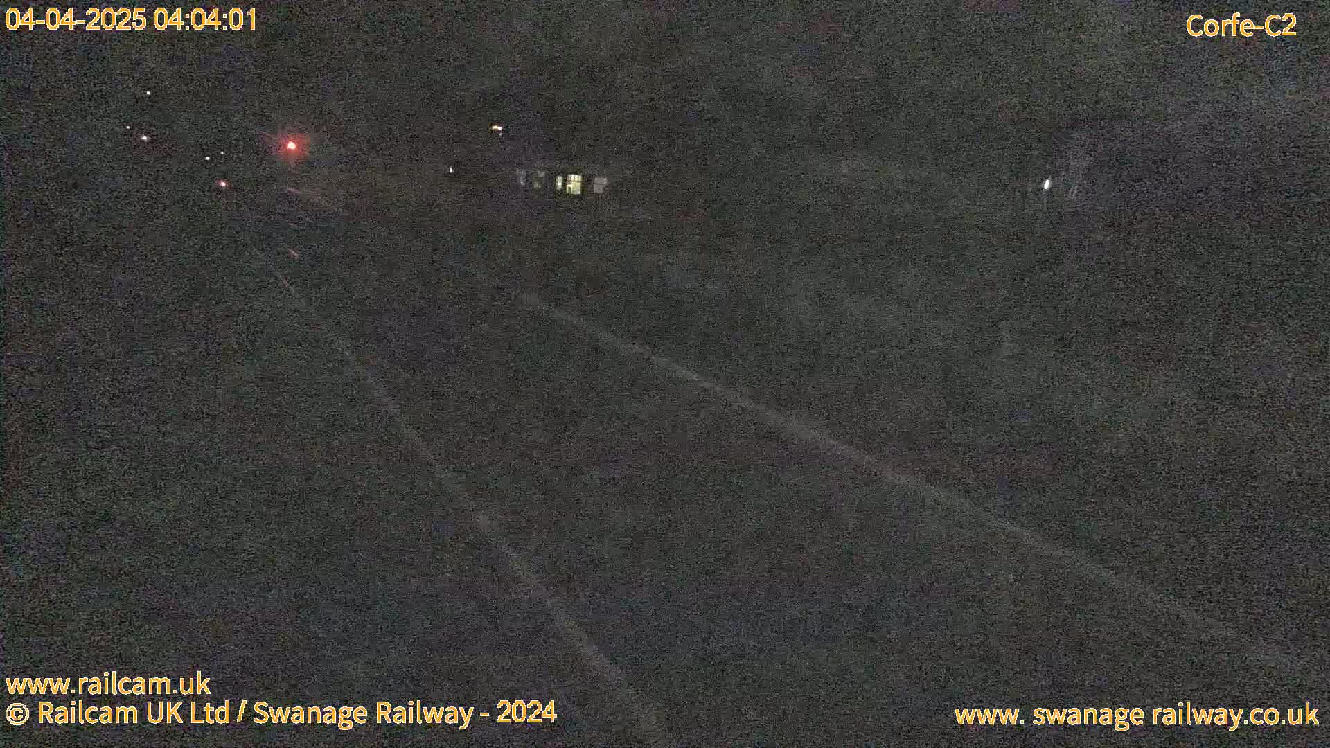 A dark, nighttime view of a railway track with faint lights visible in the distance.