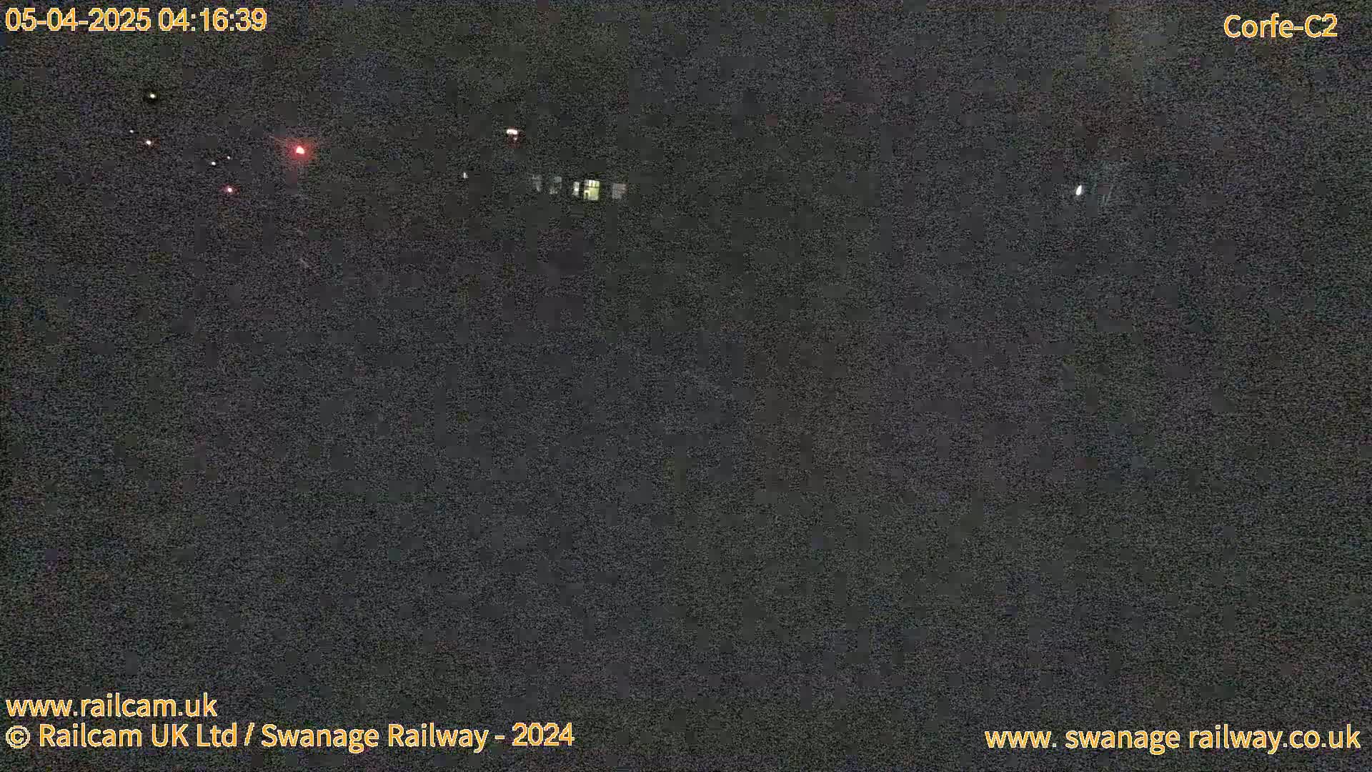 A nighttime, dark outdoor scene shows a few faint lights in the distance.