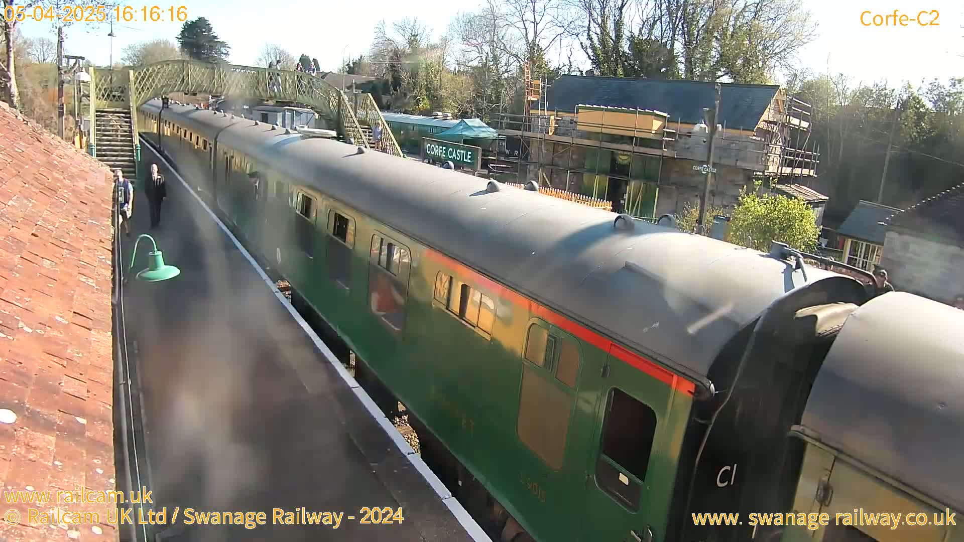 A long green passenger train sits at a station on a sunny day.