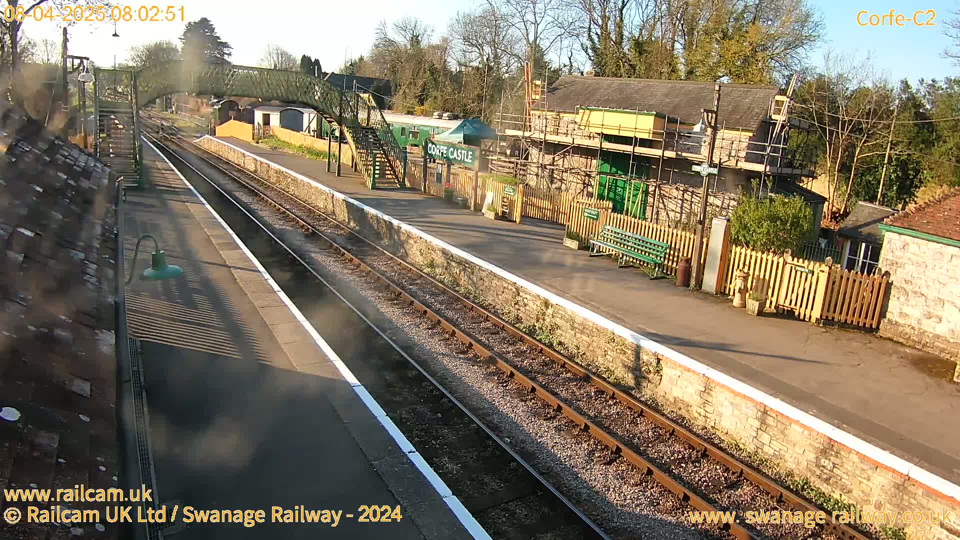 A sunny railway station with a train carriage and a building under construction is seen from a high vantage point.