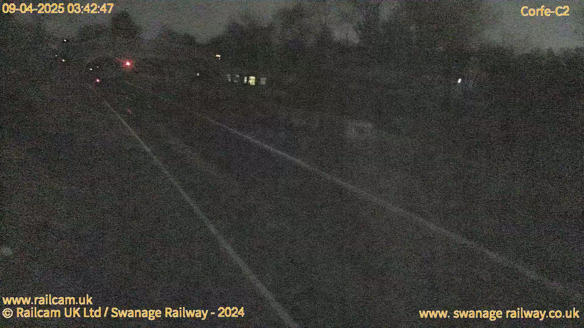 A dark, nighttime view of a long, straight road with faint white lines and a few distant lights.