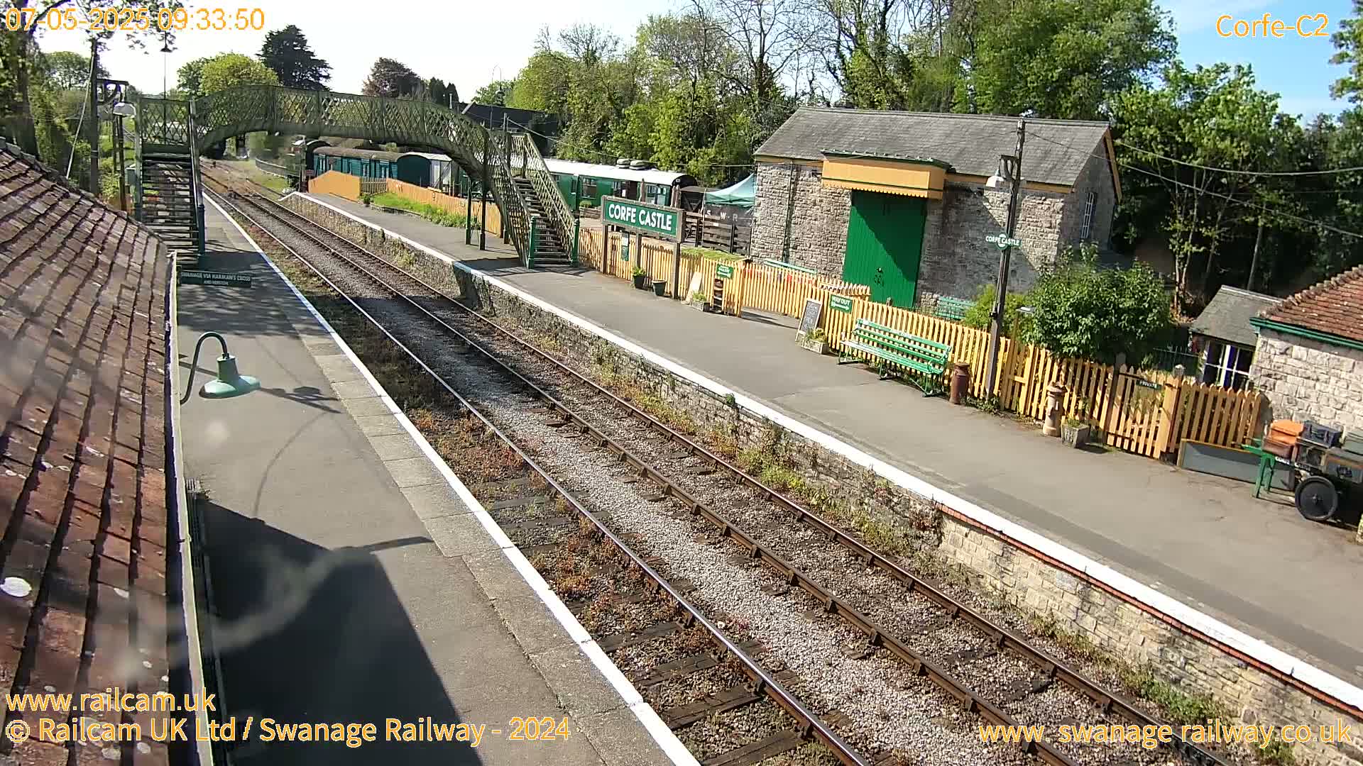A sunny view of a train station with railway tracks, platforms, and station buildings.
